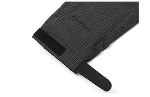 Vue rapprochée d'un tissu noir à motif quadrillé avec une sangle velcro et une languette de traction, rappelant les matériaux robustes que l'on retrouve dans la veste de randonnée coupe-vent pour homme Simwood "SIMWOOD - SM130288".